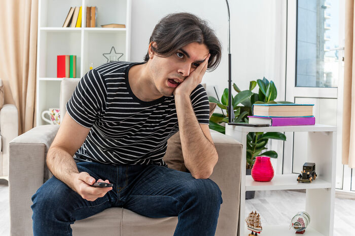 Young man in striped shirt looking frustrated while sitting on couch, reflecting tension in a relationship involving financial disputes.