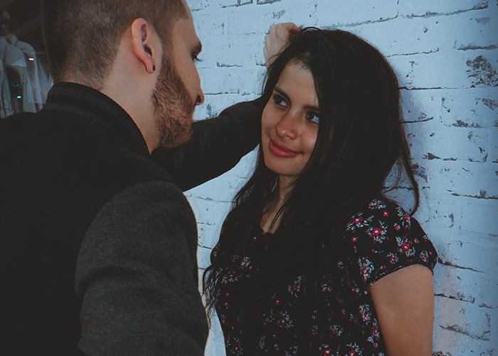 Man leaning against a wall talking to a woman in a floral dress.