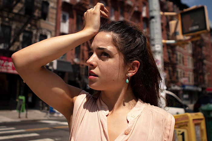 A woman on a European street shielding her eyes from the sun, highlighting strange aspects of European daily life.
