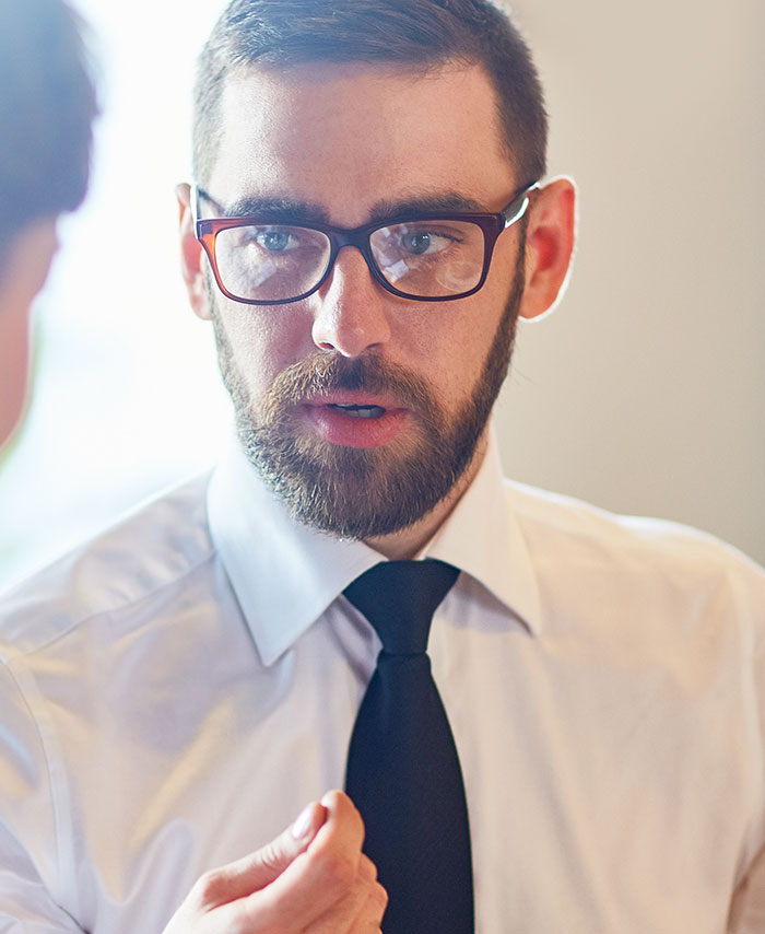A man with glasses and a tie engaging in a business discussion, related to traders' arrogance and turning the tables.