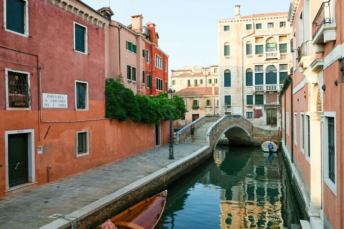 Peaceful Venice canal scene with colorful buildings and a small bridge reflecting in the water.