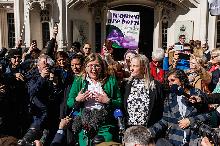 People gathered outside a UK court holding signs amid media presence, related to J.K. Rowling's trans rights stance. People gathered outside a UK court holding signs amid media presence, related to J.K. Rowling's trans rights stance.