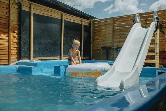 Young boy sitting on a float in a backyard pool with a slide, illustrating lifesaving and drowning prevention themes.