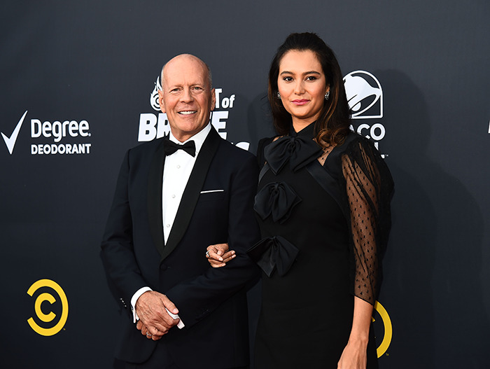 Bruce Willis with his wife on a red carpet in formal attire, smiling for a photo together. Bruce Willis with his wife on a red carpet in formal attire, smiling for a photo together.
