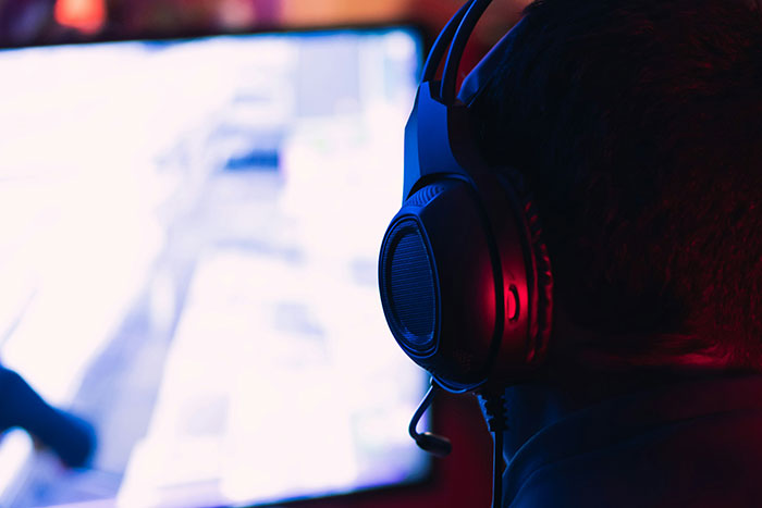 Person wearing headphones, facing a blurred screen in a dimly lit room, highlighting the impact of business decisions.