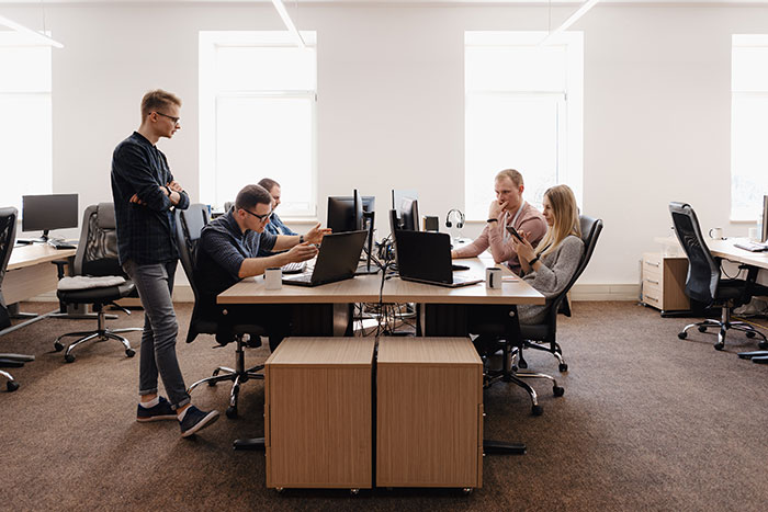 Team of office workers collaborating at desks with laptops and computers in a modern workspace showing company teamwork.