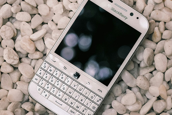 BlackBerry smartphone with physical keyboard resting on white pebbles representing companies affected by bad decisions