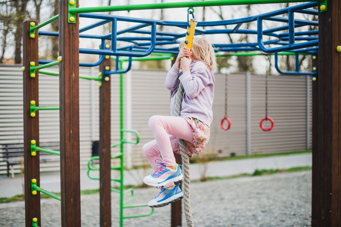 Child climbing a rope on a colorful swing set at playground, highlighting woman buying swing set for her kid.