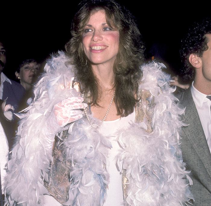 Smiling woman in a glamorous white feather outfit at an event, embodying Hollywood beauty style.