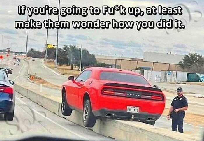 Red sports car stuck on a road divider, with a police officer observing, capturing a humorous car meme moment.
