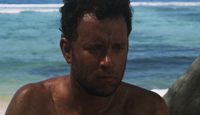 Actor showing physical and emotional dedication to difficult roles, sitting shirtless by the ocean with a serious expression.