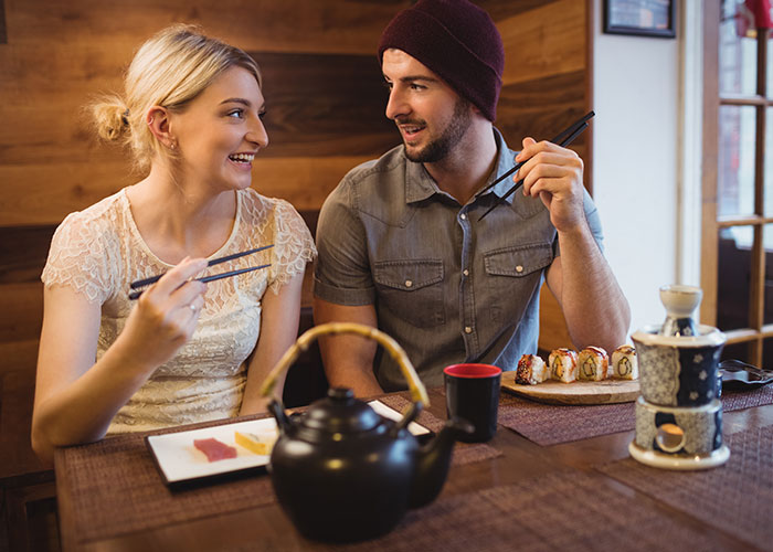 Couple enjoying sushi together at a restaurant, smiling and using chopsticks.