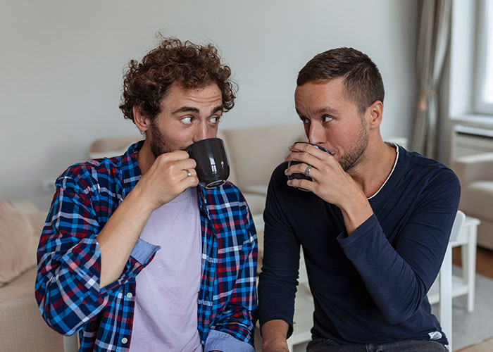 Two men sitting indoors, sharing secrets over coffee, illustrating themes of temptation and infidelity.