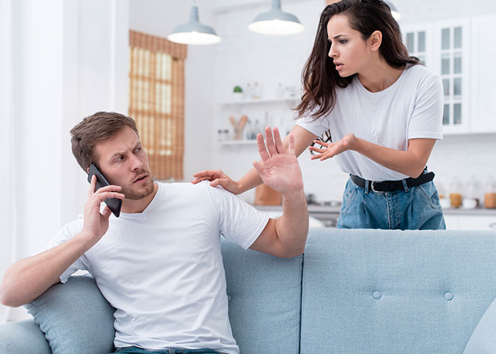 Couple in tense discussion, man on phone looks guilty, woman expresses frustration, illustrating temptation and infidelity.