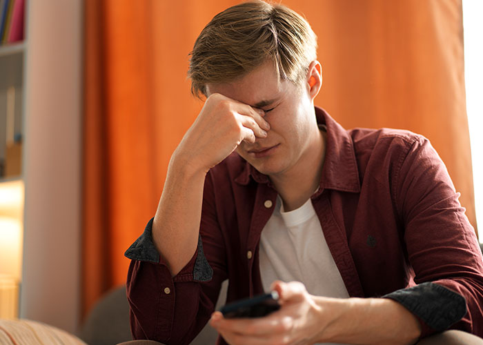 Young man in distress, wearing a red shirt, holding a phone, symbolizing temptation and the act of cheating.