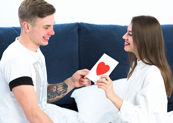 A couple smiling at each other, exchanging a card with a heart, representing temptation and relationships.