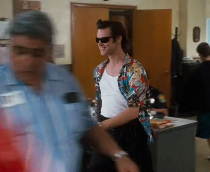 Talented celebrity wearing sunglasses and a colorful shirt, walking through a busy office setting.