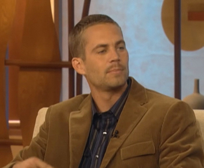A person sitting in an interview, dressed in a brown jacket and striped shirt.