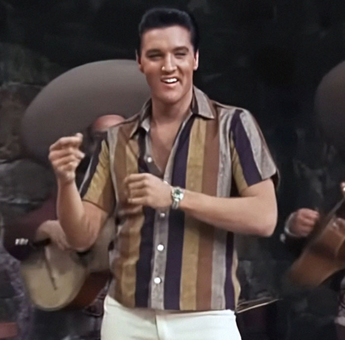 Person in a striped shirt performing energetically, with musicians playing in the background.