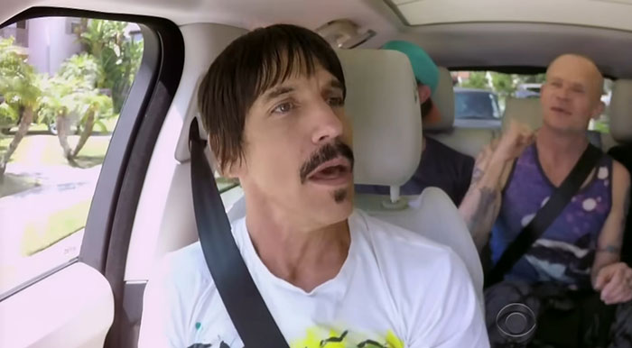 A man with a mustache and short hair singing in a car with others, highlighting talented people.
