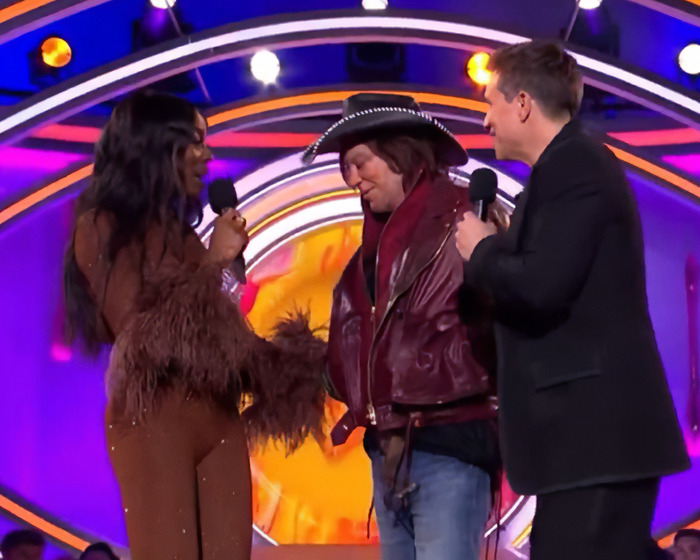 AJ Odudu and two others on Celebrity Big Brother stage, engaging with each other.