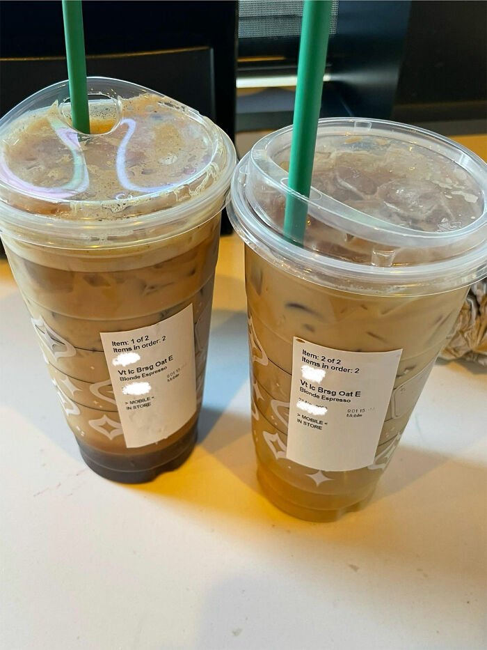 Two iced coffees from a chain restaurant with green straws and order labels on a table.