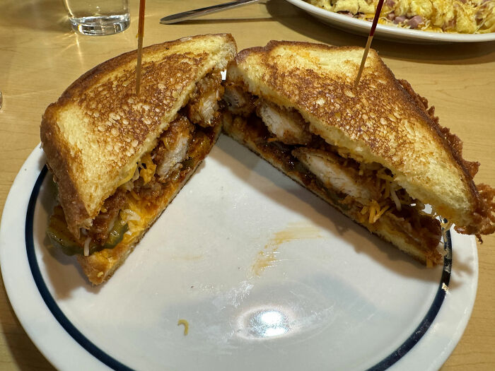 Grilled sandwich with crispy chicken, cheese, and sauce on a white plate at a chain restaurant.