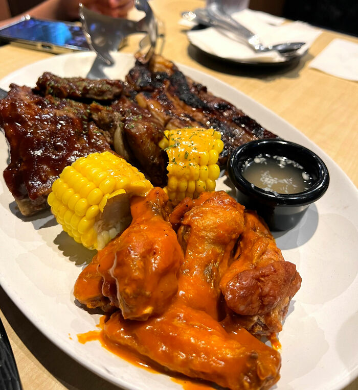 Plate of chain restaurant dishes with ribs, corn, buffalo wings, and sauce.