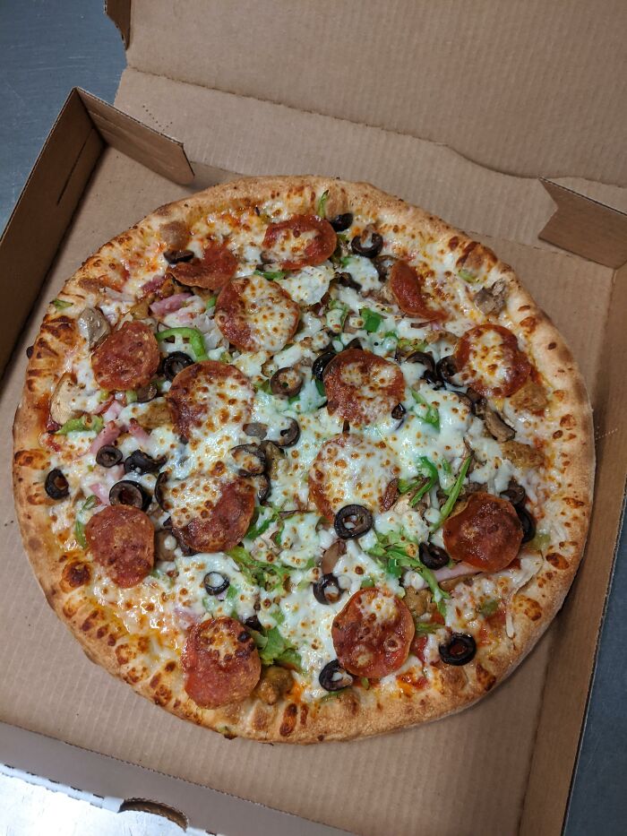 Chain restaurant pizza topped with pepperoni, olives, and green peppers in a cardboard box.