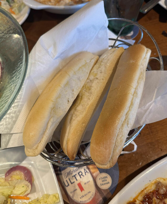 Three breadsticks in a basket at a chain restaurant, served with salad and pasta dishes.