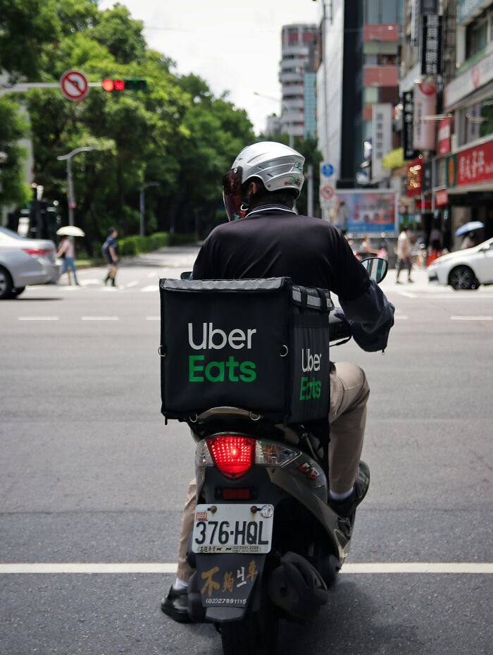 Uber Eats delivery driver on a scooter, highlighting chain restaurant practices in urban setting.