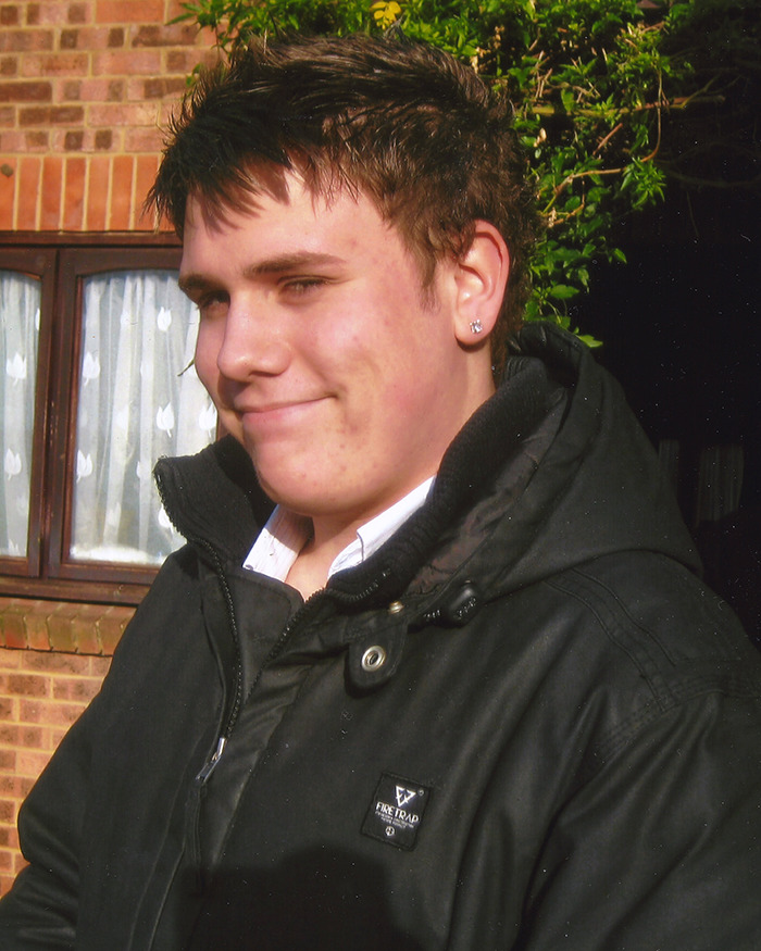 Young actor wearing a black jacket, standing outside a brick building.
