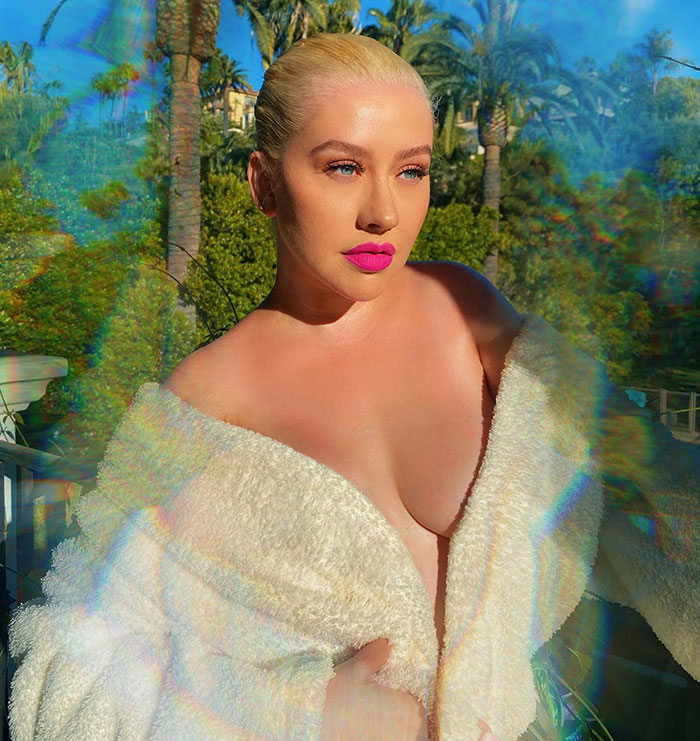 Christina Aguilera in outdoor photoshoot wearing white robe with bold pink lipstick and edited effects on the image