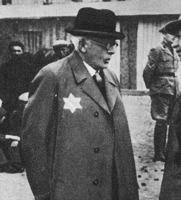 An elderly man wearing a coat with a star, representing historical traitors, in a black-and-white photograph.