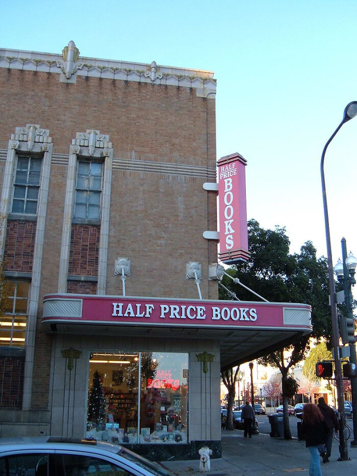 Half Price Books store exterior with street view and signage, featuring trees and pedestrians nearby.