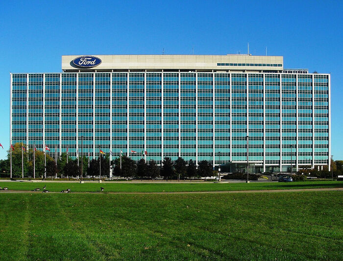 Ford headquarters building under clear sky, reflecting sunlight on glass facade.
