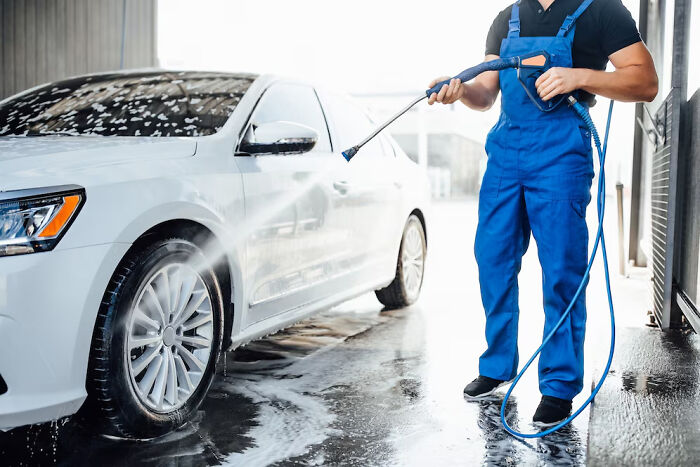 Man wearing blue overalls washing a white car with a hose, illustrating small things that saved lives.