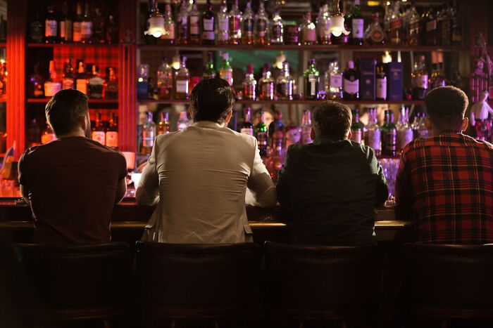 Four people sitting at a bar with bottles on shelves, illustrating small things that unexpectedly saved lives.