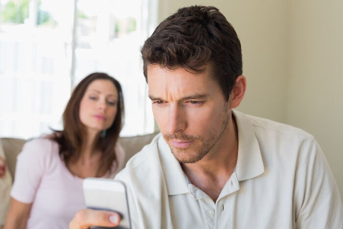 Man intently reading questions on phone, with curious woman in background, highlighting inquiries doctors face.