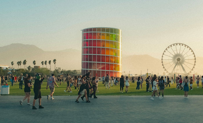 Festival-goers at Coachella with colorful tower and Ferris wheel, capturing the event's vibrant music vibes.