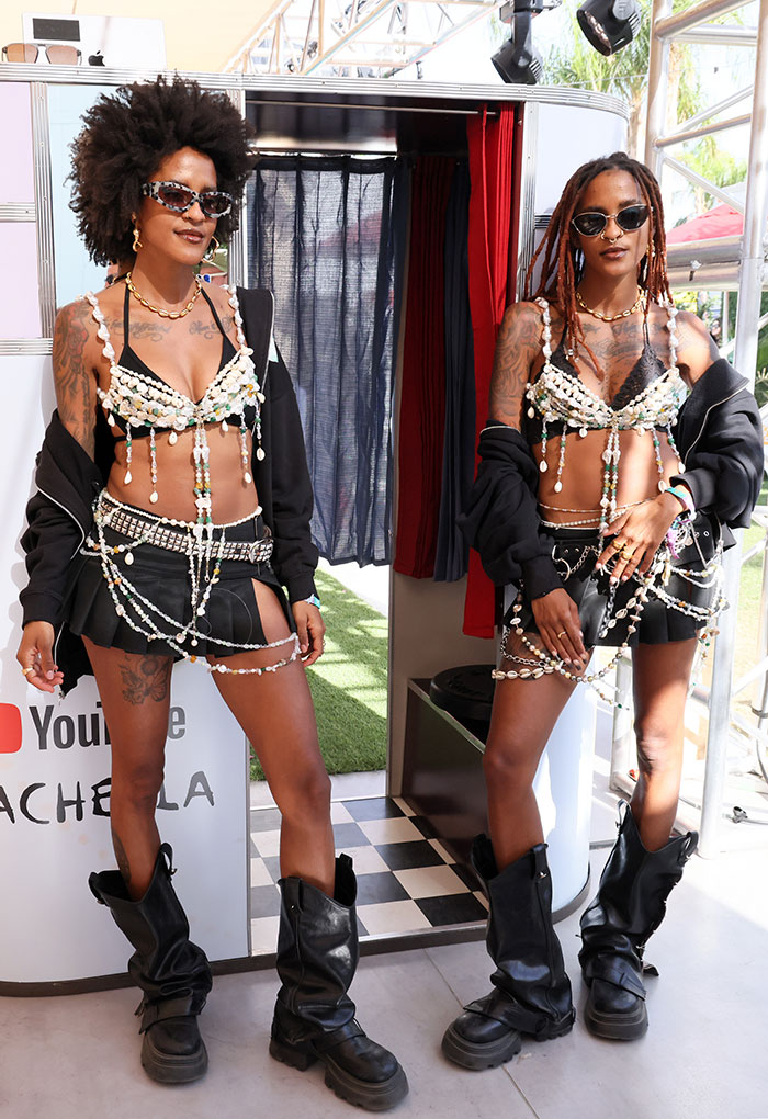 Celebrities in bold outfits at Coachella 2025, wearing pearl-decorated tops, black boots, and sunglasses, standing by a booth.