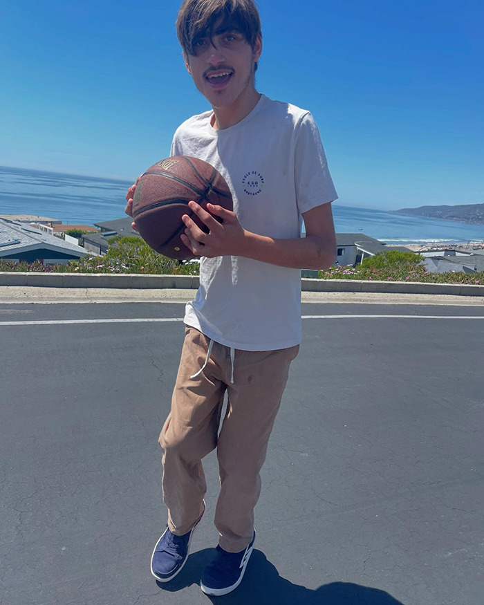 Young man holding a basketball by the ocean, related to Colin Farrell's 21-year-old disabled son and his care facility decision.