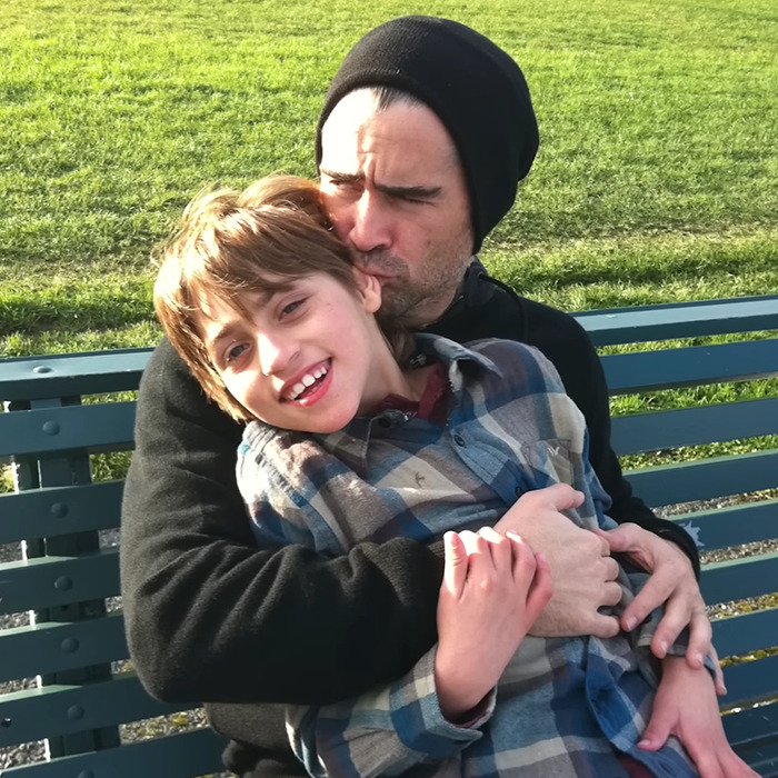 Father embracing son on a bench outdoors, displaying affection and care.