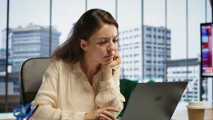 Woman on video call, looking concerned, overhearing coworkers' comments in an office setting.