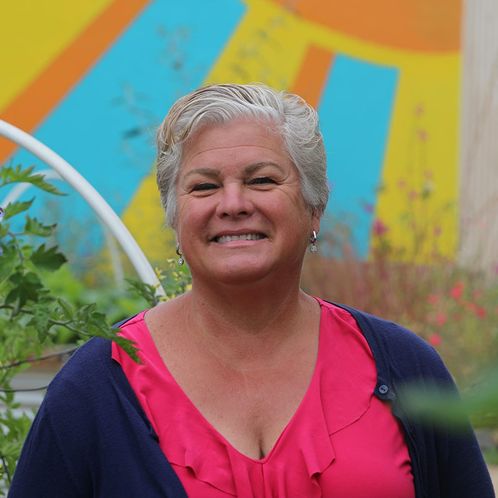 Smiling person standing outdoors with colorful mural, relevant to trans locker room discussion.