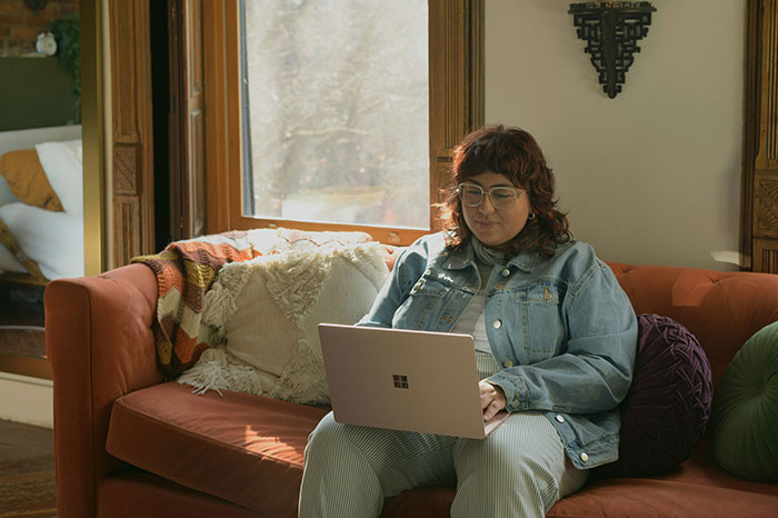 Person working on a laptop, sitting on a couch, highlighting company care through remote work perks.