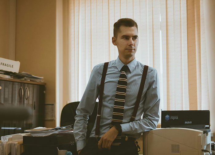 Employee in formal attire with suspenders, standing beside an office printer, highlighting work perks.