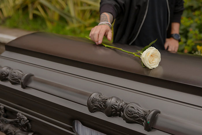 A hand places a white rose on a coffin, symbolizing compassionate employee perks and care.