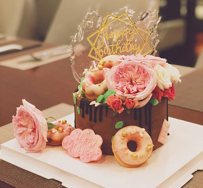 A decorative birthday cake adorned with pink flowers and donuts, showcasing company care for employees.