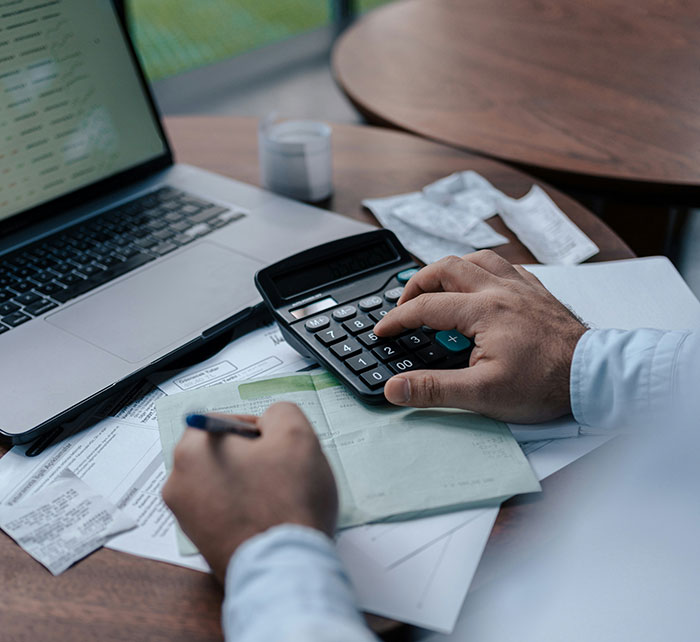 Person calculating expenses at a desk with a laptop, depicting employee work perks and company care.